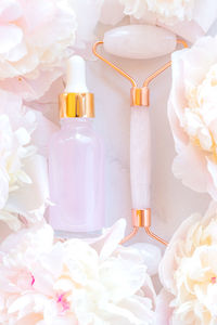 Face massage roller with natural essential oil in pipette bottle on marble background with peonies.