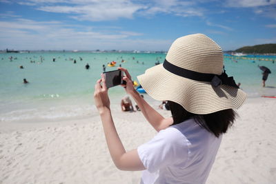 Rear view of woman photographing on beach
