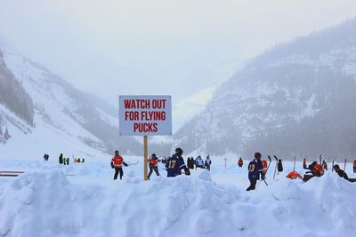 People playing ice hockey by snowcapped mountains during winter 