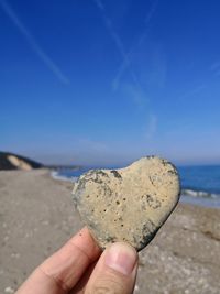 Close-up of hand holding rock on beach against sky