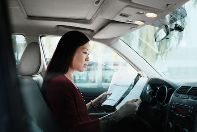 Side view of woman holding documents while sitting in car