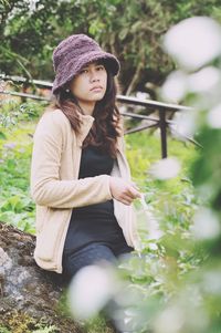 Bored woman wearing hat sitting on rock amidst grassy field