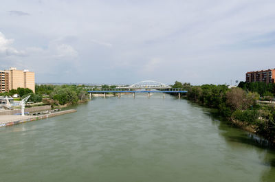 Bridge over river by buildings against sky