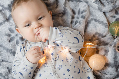 A baby boy lies on the bed and plays with a christmas garland.