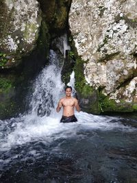 Portrait of shirtless man in waterfall