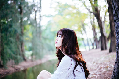 Side view of thoughtful young woman sitting in forest