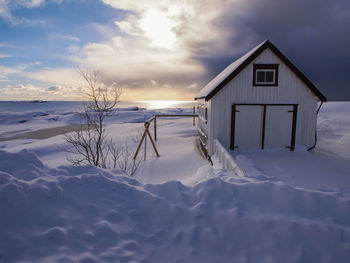 House on snow covered landscape against sky