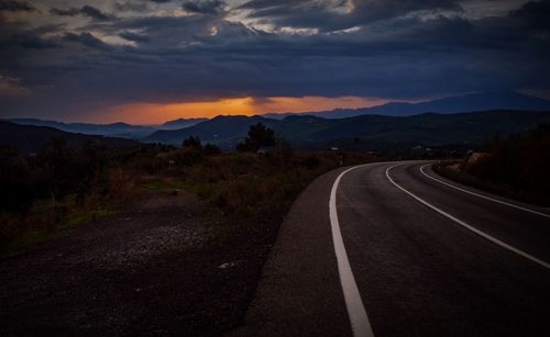 Empty road leading towards mountains against sky during sunset