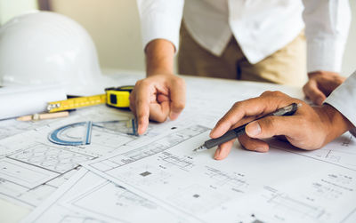 Cropped image of architects discussing blueprint on table
