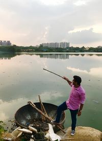 Rear view of man fishing in lake against sky