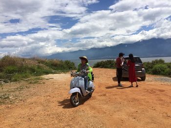 Rear view of people sitting on landscape against cloudy sky