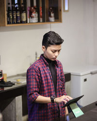 Side view of young man using mobile phone while standing in workshop