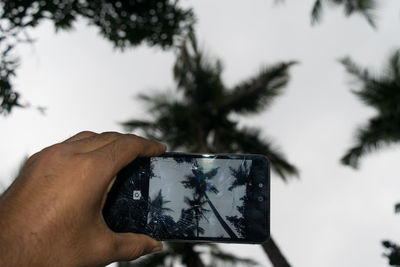 Close-up of hand holding mirror against sky