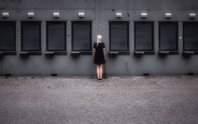 Rear view of woman standing amidst shutters on wall