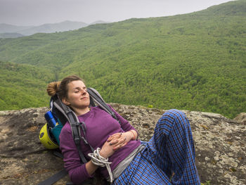 Portrait of smiling young woman sitting on mountain against sky