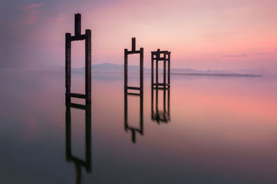 Silhouette wooden posts in sea against sky during sunset