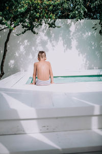 Rear view of shirtless man sitting in swimming pool