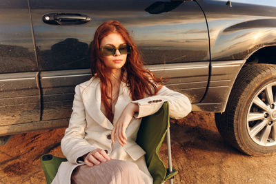 Portrait of young woman sitting on car