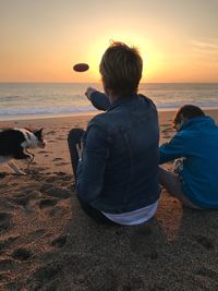 Rear view of mother with son by dog at beach against sky during sunset