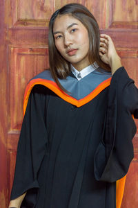 Portrait of beautiful young woman in graduation gown standing door