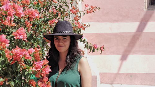 Portrait of beautiful young woman standing by pink flowering plants