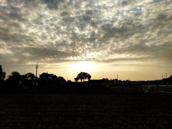 Silhouette trees on field against sky at sunset