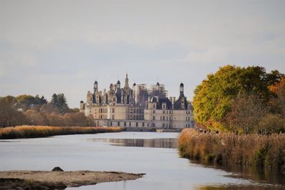 Buildings at waterfront against cloudy sky