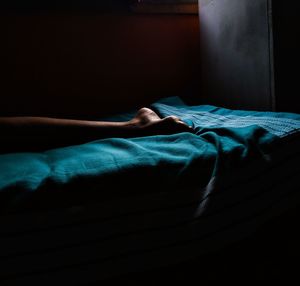 Low section of person sleeping on bed in darkroom