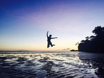 Silhouette man jumping in sea against sky during sunset
