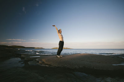 Shirtless transgender man standing on coast with raised arm