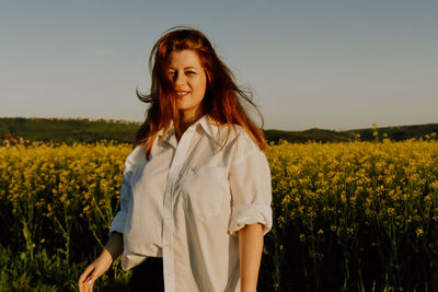 Young woman standing amidst yellow flowering plants on field against sky