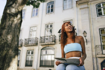 Young woman with map sitting in front of building