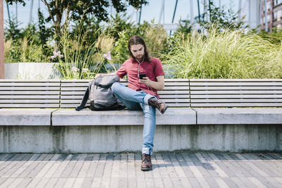 Man sitting on a bench with earbuds using cell phone