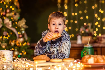 Portrait of boy sitting on table at christmas tree