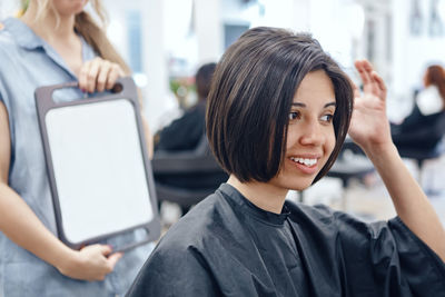 Beautician holding mirror for customer in salon