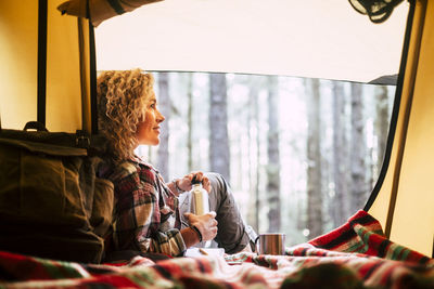 Woman sitting by tent with coffee cup in forest