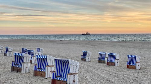 Chairs on beach against sky during sunset