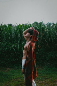 Full length of shirtless man standing on field against sky