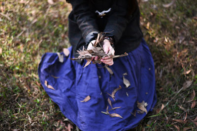 Low section of woman holding dry leaves on field