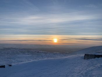 Snow covered landscape against sky during sunset