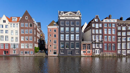 Buildings by river against blue sky