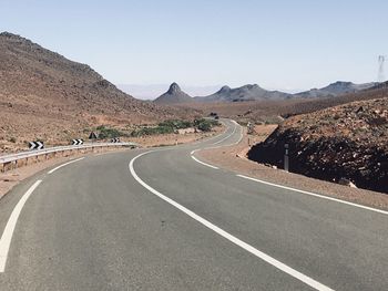 Road leading towards mountains against clear sky