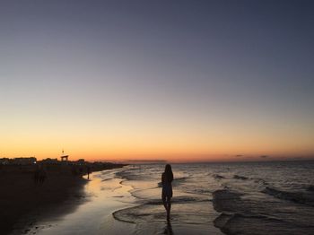 Silhouette woman standing on beach against clear sky during sunset