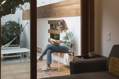 Woman reading book sitting on chair at patio