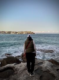 Rear view of man standing at beach against clear sky