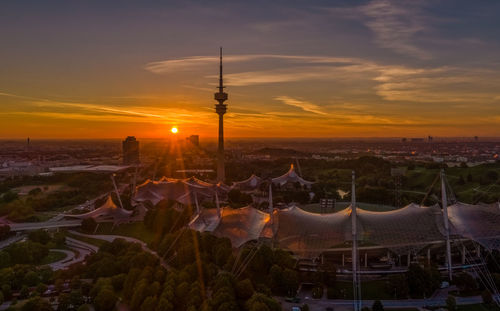 Communications tower in city against sky during sunset