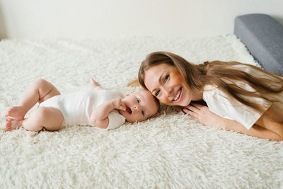Caucasian mom lies on the bed with her baby son and smiles happily
