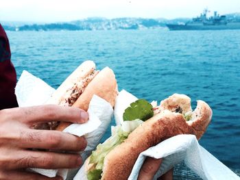 Cropped image of hands holding sandwich against sea