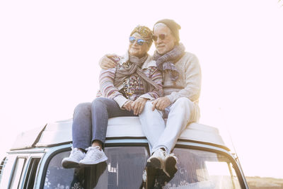 Smiling senior couple sitting on van against sky