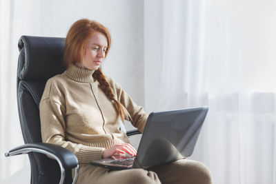 Woman using mobile phone while sitting on chair